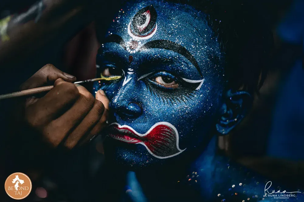 A devotee gets intricate facial painting as he starts transforming to resemble a deity or demon. Cossimbazar, West Bengal