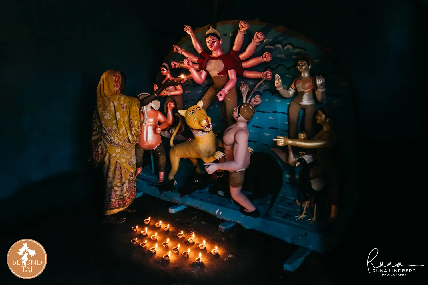 Woman lighting oil lamps before a Durga idol during evening puja