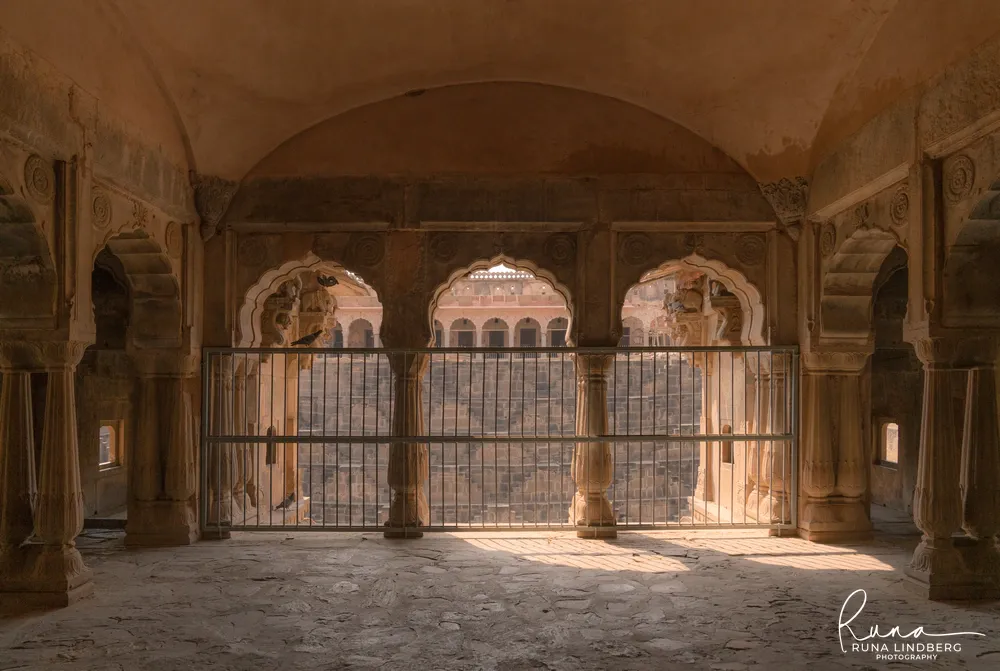 View through three scalloped arches and a metal barrier onto the stepped walls of Chand Baori stepwell in Abhaneri, Rajasthan