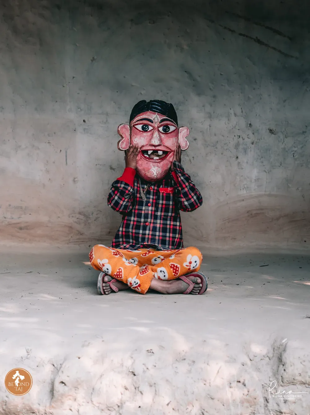Child holding a gomira mask in front of a clay wall