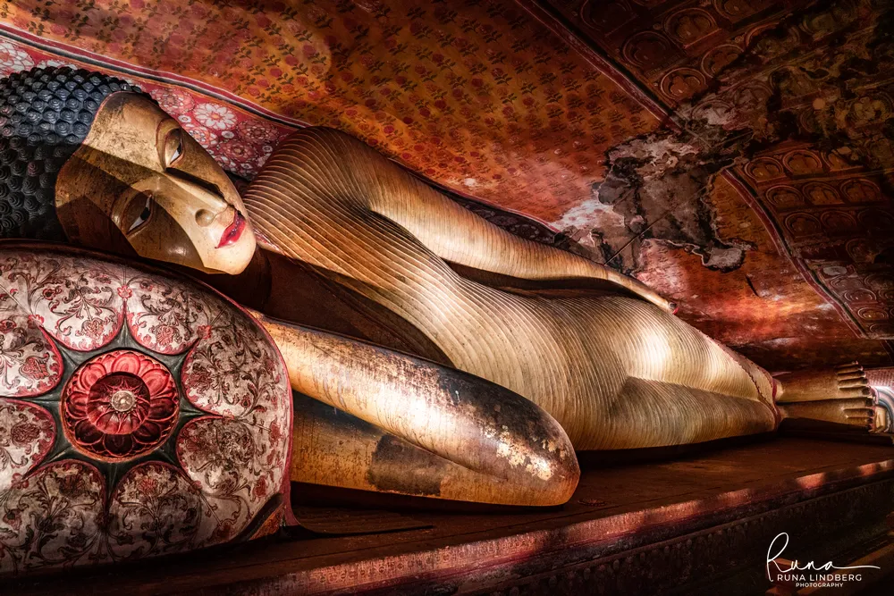 Close view of a gilded reclining Buddha's head on a decorated bolster beneath an ornate red and gold ceiling at Dambulla
