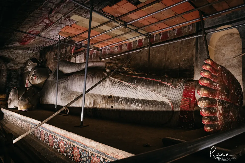A large reclining Buddha behind restoration scaffolding at Dambulla, the soles of its feet painted red