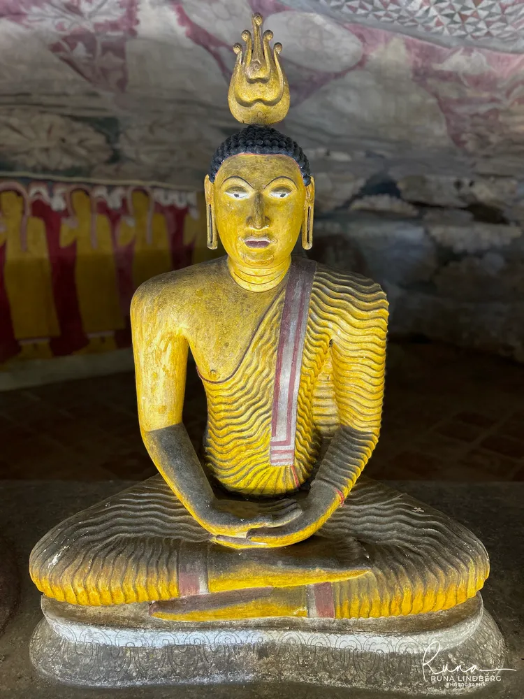 A single seated Buddha in meditation with a flame finial, painted in ochre with wavy robe folds, at Dambulla