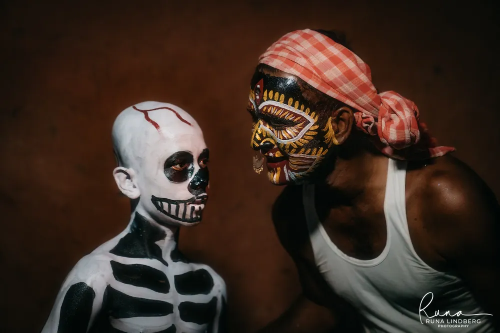 Boy painted as a skeleton and a man with a red, yellow and white painted face and a checked headcloth facing each other, Gajan festival, Gangatikuri, West Bengal