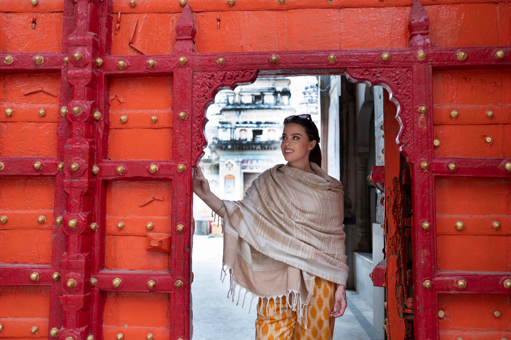 Runa Lindberg in a cream shawl stepping through the arched opening of the red, brass-studded door of the Rangji Temple, Pushkar