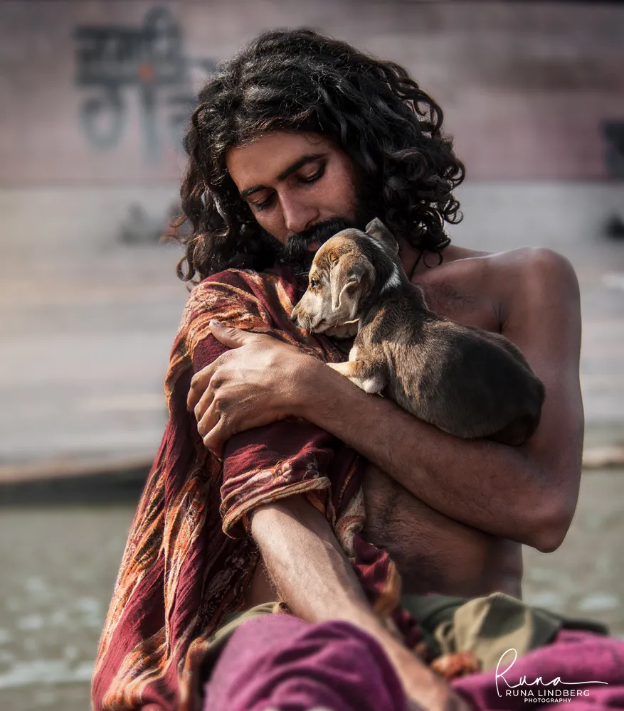 Young man with long curly hair cradling a puppy against his chest on the ghats of Varanasi